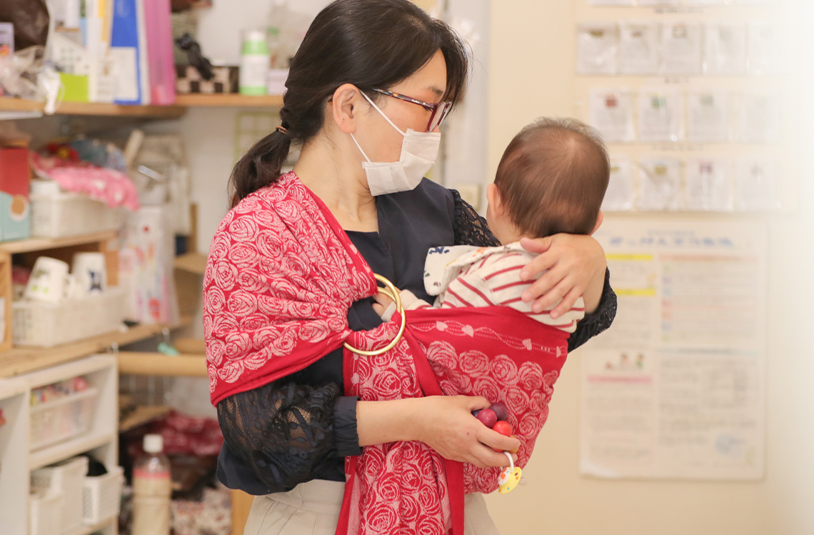 スリングで赤ちゃんを抱き抱えている大久保久美子さんの写真。